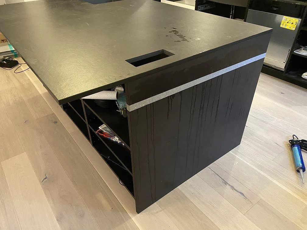 Köksö i mörk Dekton Sirius keramik sedd från sidan med öppna stommar under, i ett kök i Oxie under montering.