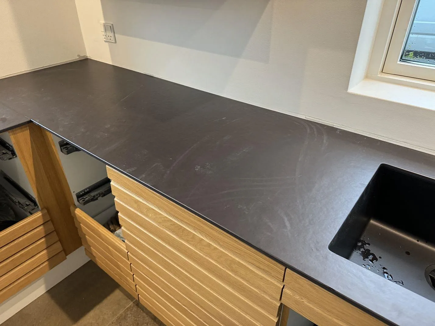 Köksbänkskiva i matt Dekton Sirius med svart diskho och träinredning i ett kök i Roskilde.