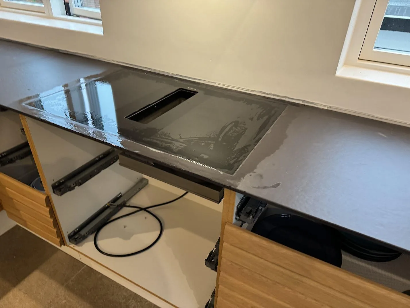 Köksbänkskiva i matt Dekton Sirius med mörk Miele-häll och öppna skåpstommar i Roskilde.