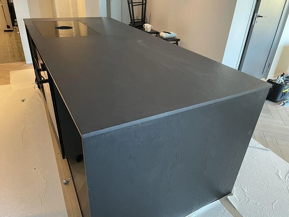 Köksö i Dekton Sirius med rak kant och nedfälld fläkt sedd från gaveln, matt mörk keramikbänkskiva i ett kök i Särö.