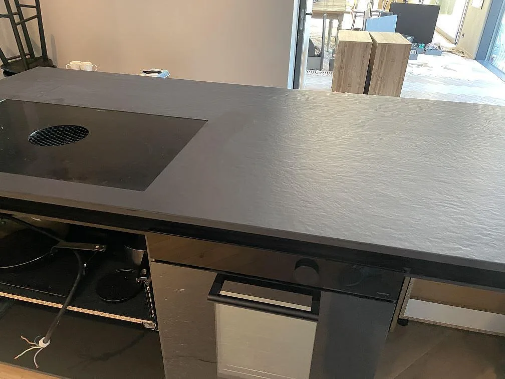 Köksö i mörk Dekton Sirius med nedfälld induktionshäll och rund integrerad fläkt, matt keramikyta i ett kök i Särö.