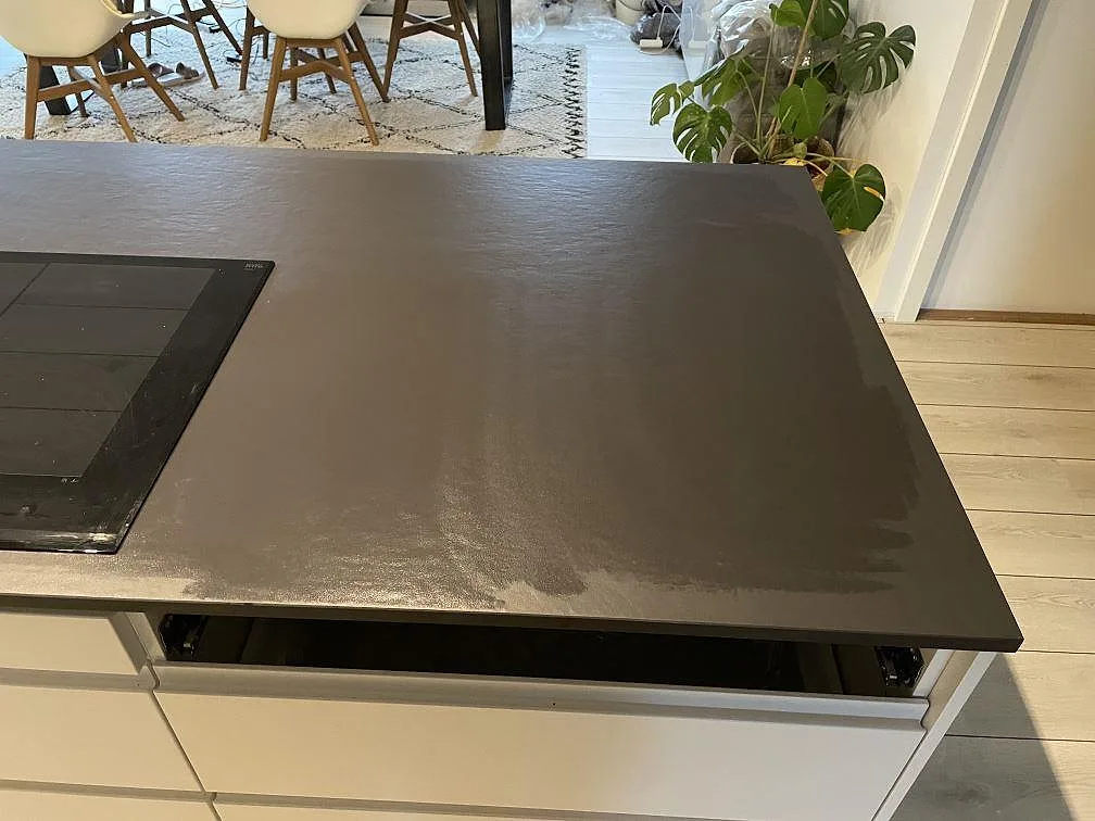 Köksbänkskiva i mörkt grå Dekton Sirius, matt betongliknande keramik, på en fristående köksö med infälld induktionshäll i ett kök i Stenløse.