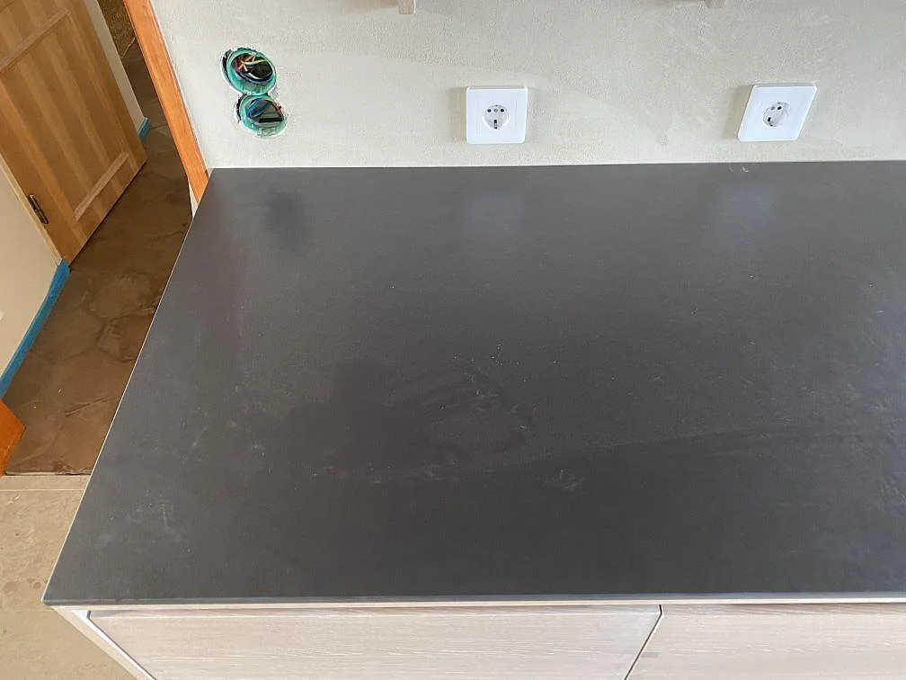 Perimeterbänk i matt Dekton Sirius mot vägg med eluttag, mörk keramikbänkskiva i ett kök i Svanesund.