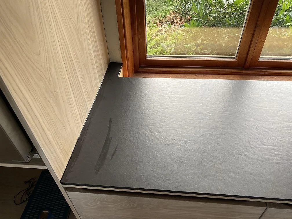 Djup fönsterbänk i matt Dekton Sirius keramik vid ett träfönster i ett kök i Svanesund.