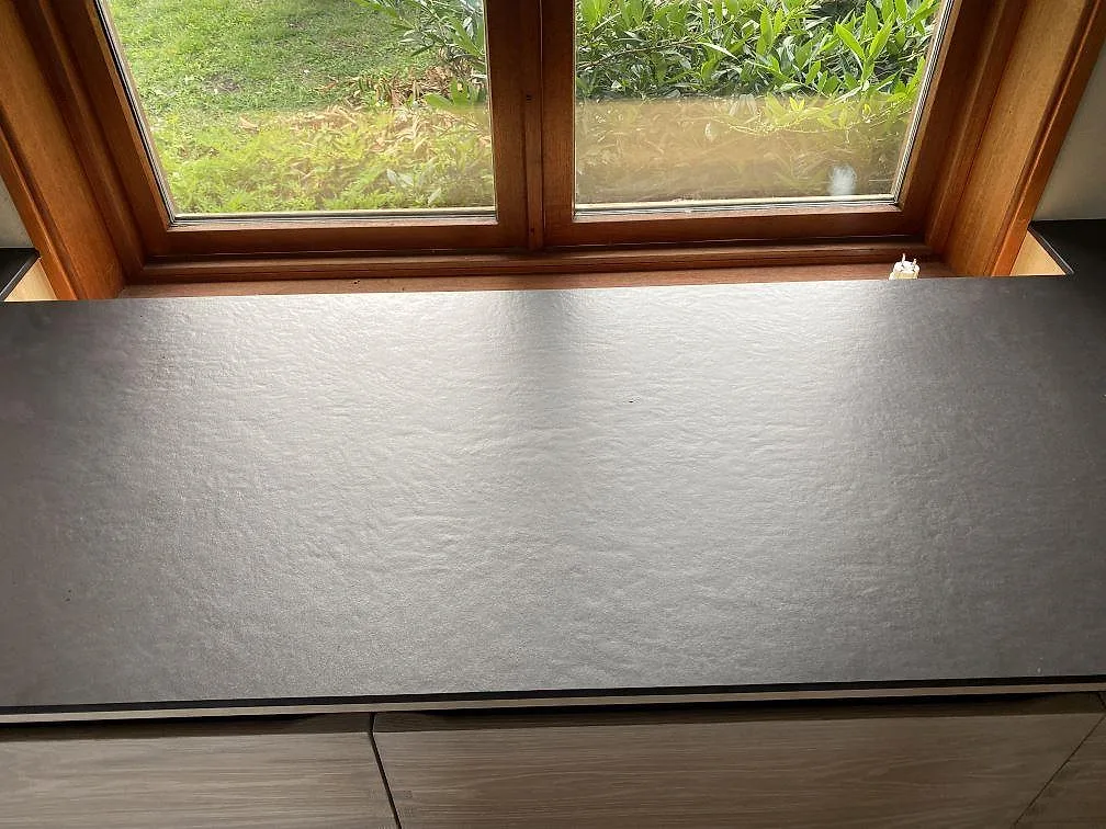Fönsterbänk i matt mörk Dekton Sirius keramik framför ett träfönster i ett kök i Svanesund.