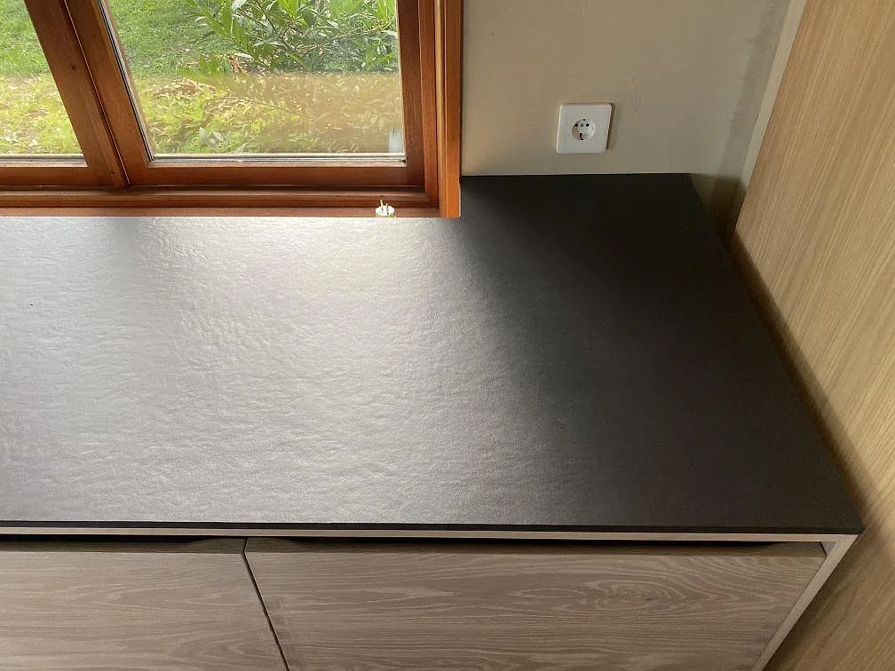 Köksbänk i matt mörk Dekton Sirius keramik i en fönsternisch med träfönster i ett kök i Svanesund.