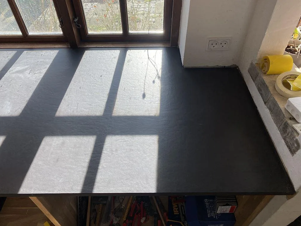 Hörnande köksbänkskiva i mörk Dekton Sirius med diskho och hällurtag i ett kök under montering i Tølløse.