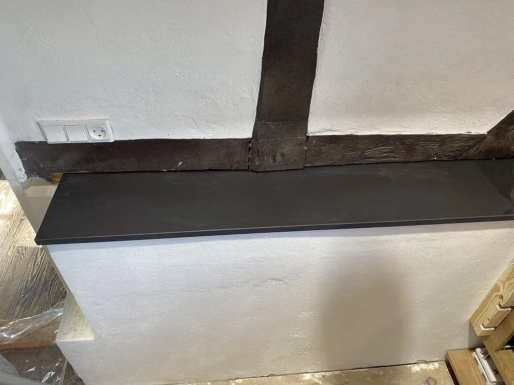 Bänkrad i matt Dekton Sirius under fönstret med solljus över den mörka stenytan i ett kök i Tølløse.
