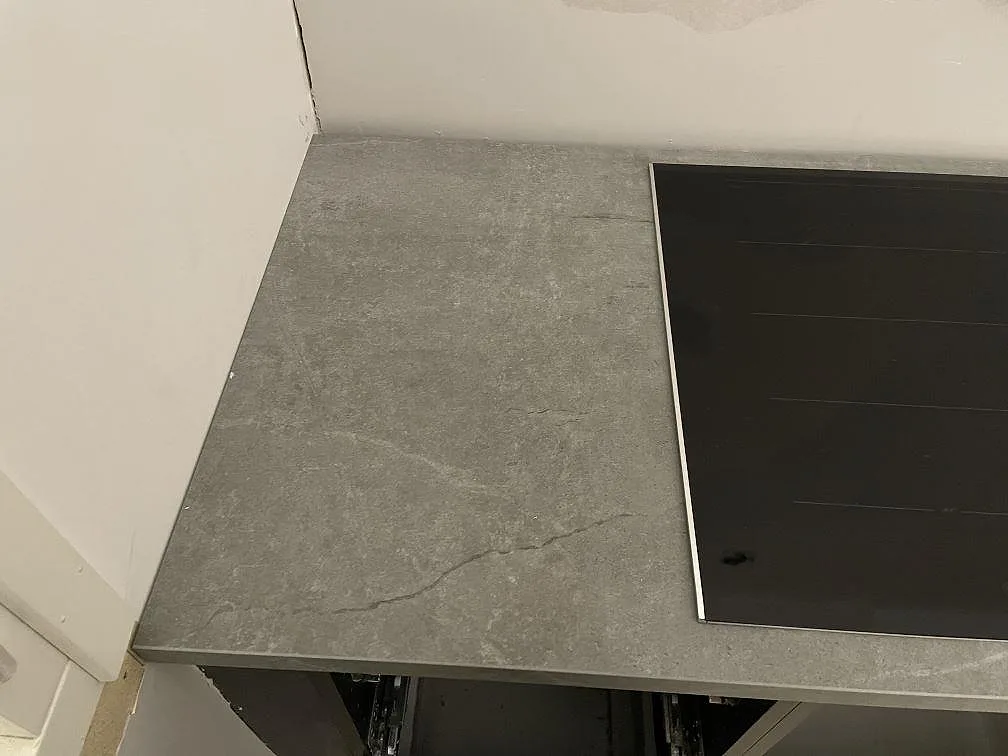Hörn av köksbänk i grå Dekton Soke i matt betonglook intill övermonterad induktionshäll i Arrie.