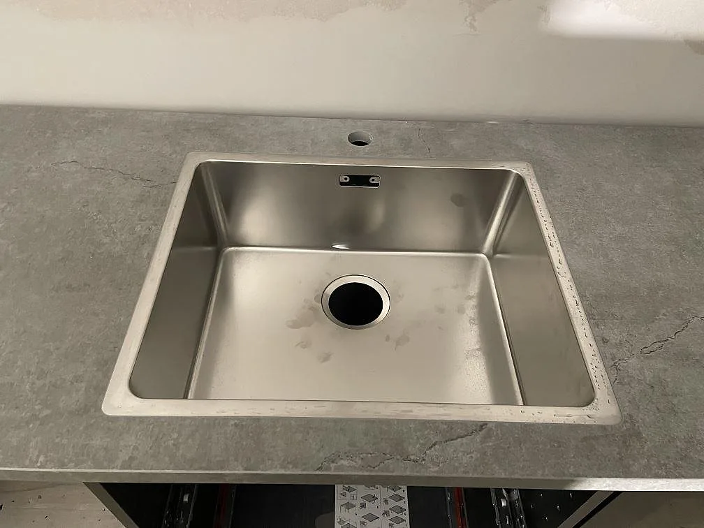 Planmonterad rostfri diskho i en köksbänk av grå Dekton Soke med matt betonglook i Arrie.