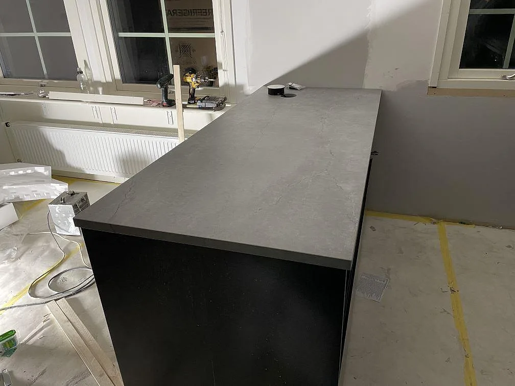 Köksö i grå Dekton Soke med matt yta och mjuk ådring, fristående bänk i ett ljust kök i Arrie.