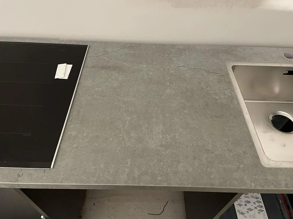 Köksbänk i grå Dekton Soke med övermonterad induktionshäll och planmonterad rostfri diskho i ett kök i Arrie.