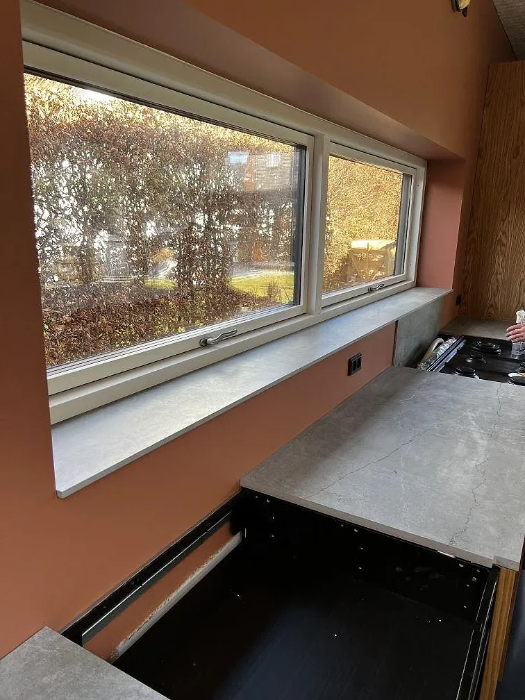 Köksbänkskiva och djup fönsterbänk i grå-beige Dekton Soke mot terrakottavägg