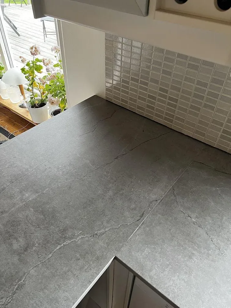 Detalj av matt Dekton Soke köksbänkskiva med grå kakelvägg och utskuren öppning i Kyrkesund.