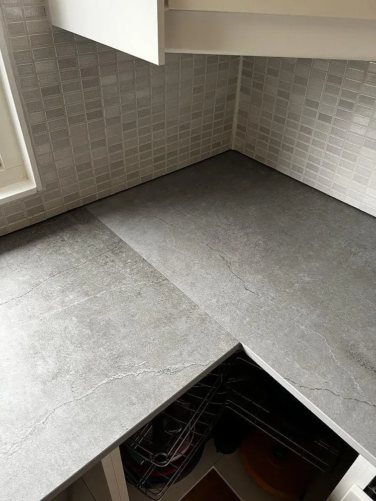 L-format hörn i köksbänkskiva av matt Dekton Soke keramik med grå mosaikkakel i Kyrkesund.