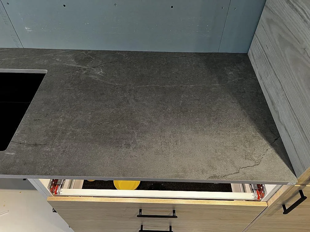Bänkskiva i Dekton Soke, matt grå keramik, med diskhoöppning och träinredning i ett kök i Löddeköpinge.