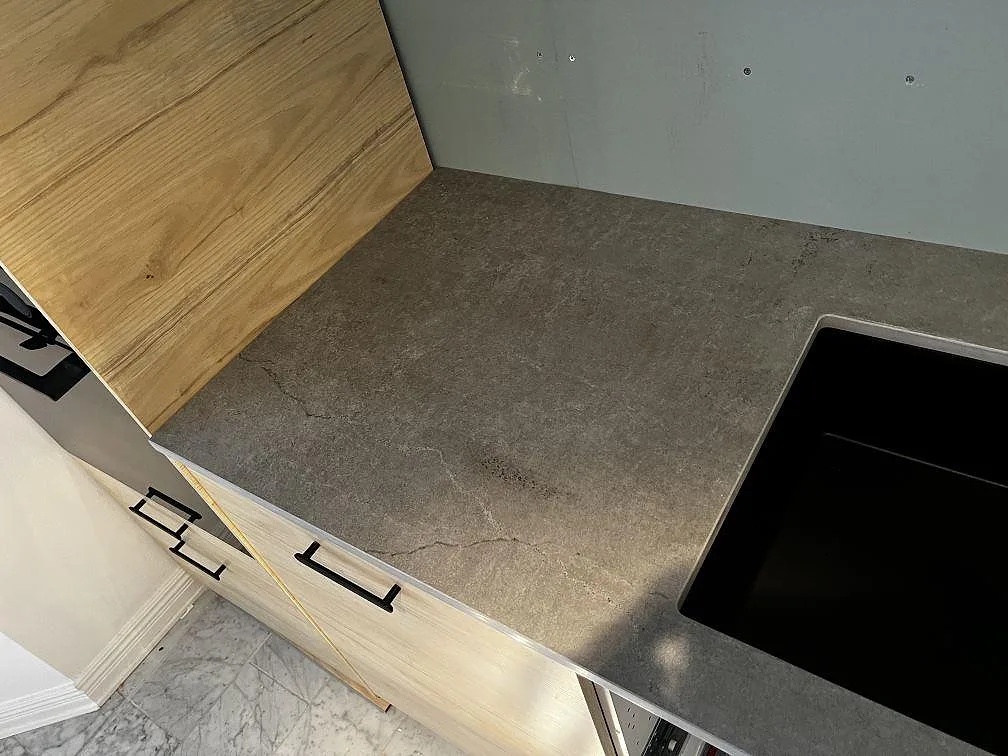 Vinklad detalj av Dekton Soke bänkskiva, matt keramik, vid svart diskho och träinredning i Löddeköpinge.