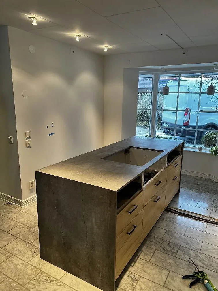 Köksö i grå Dekton Soke, matt keramik, med vattenfallssida och öppning i ett kök under montering i Löddeköpinge.