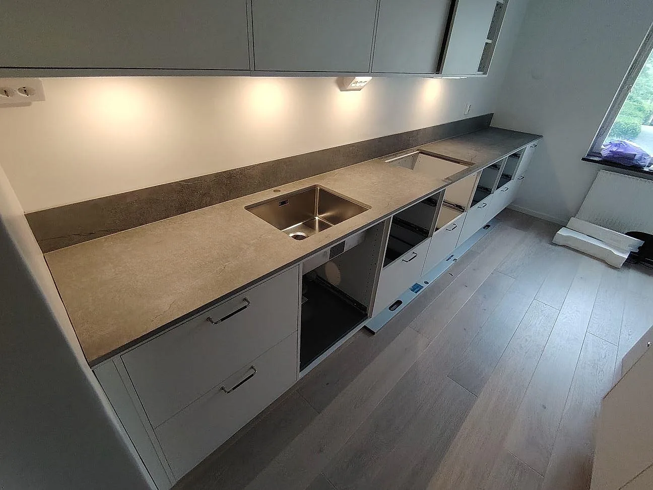Köksbänkskiva i matt gråbeige Dekton Soke i Nacka med underlimmad diskho, häll och låg stänkkant under montering.