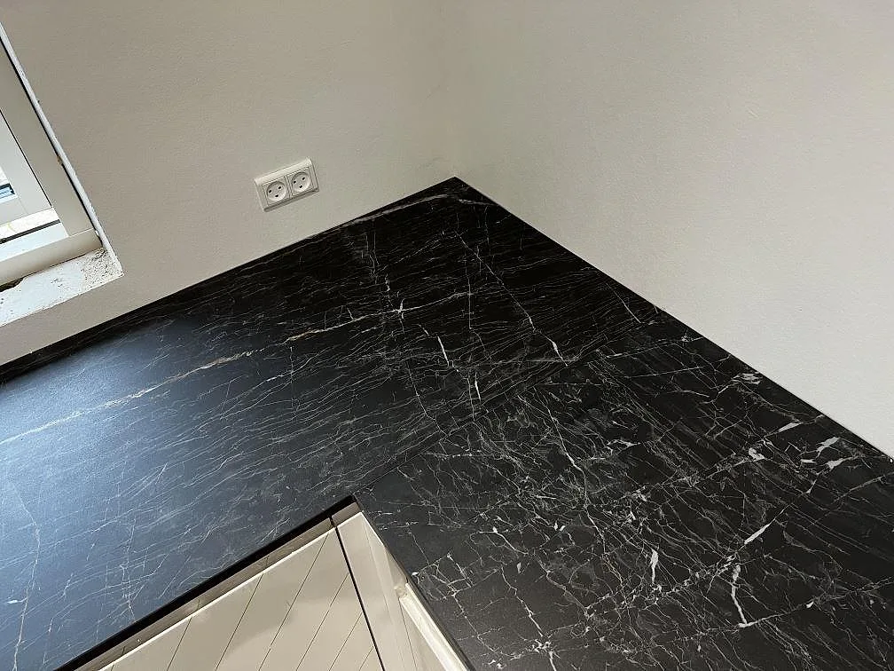 Hörnparti av polerad Dekton Somnia köksbänkskiva i svart keramik med ljus marmorliknande ådring i Ballerup.