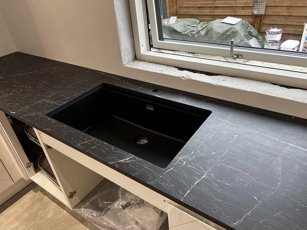 Närbild på underlimmad svart diskho i polerad Dekton Somnia köksbänkskiva med ljus ådring i Ballerup.
