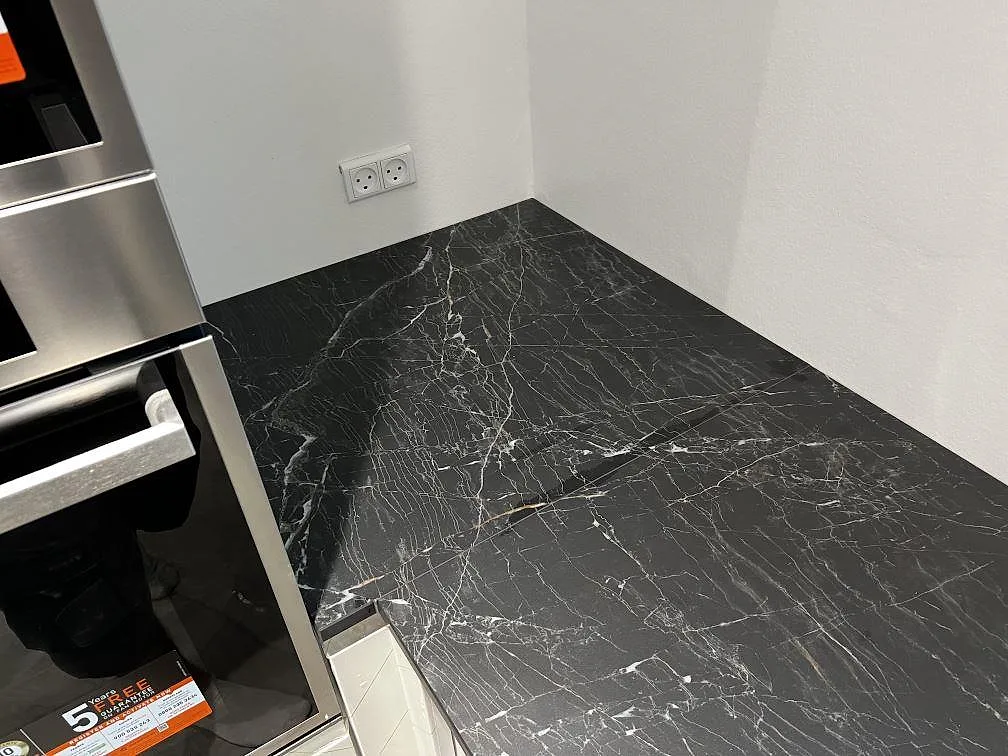 Detalj av polerad Dekton Somnia bänkskiva bredvid ugnsskåp i ett vitt kök i Ballerup.