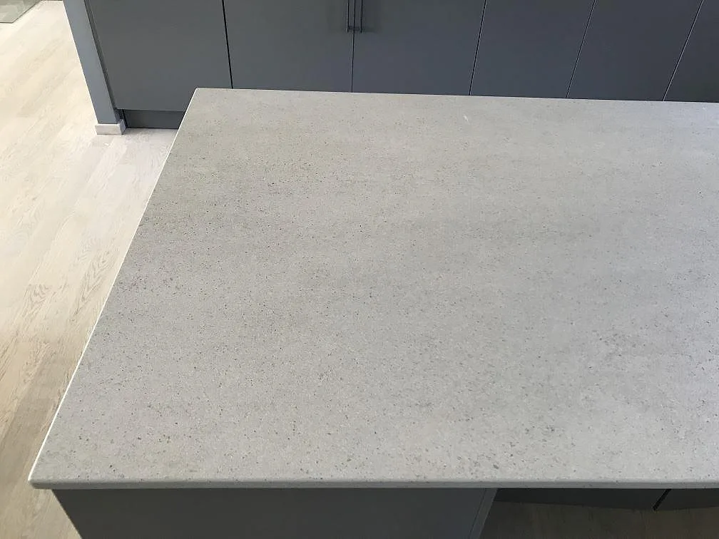 Köksbänkskiva i ljusgrå Dekton Strato, matt yta, på en köksö mot grå köksluckor i ett kök i Rydebäck.