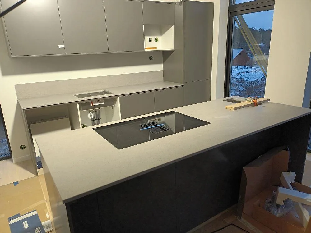 Köksbänkskiva i ljusgrå matt Dekton Strato med köksö, häll, rostfri diskho och låg stänkkant i ett kök i Svärdsklova.