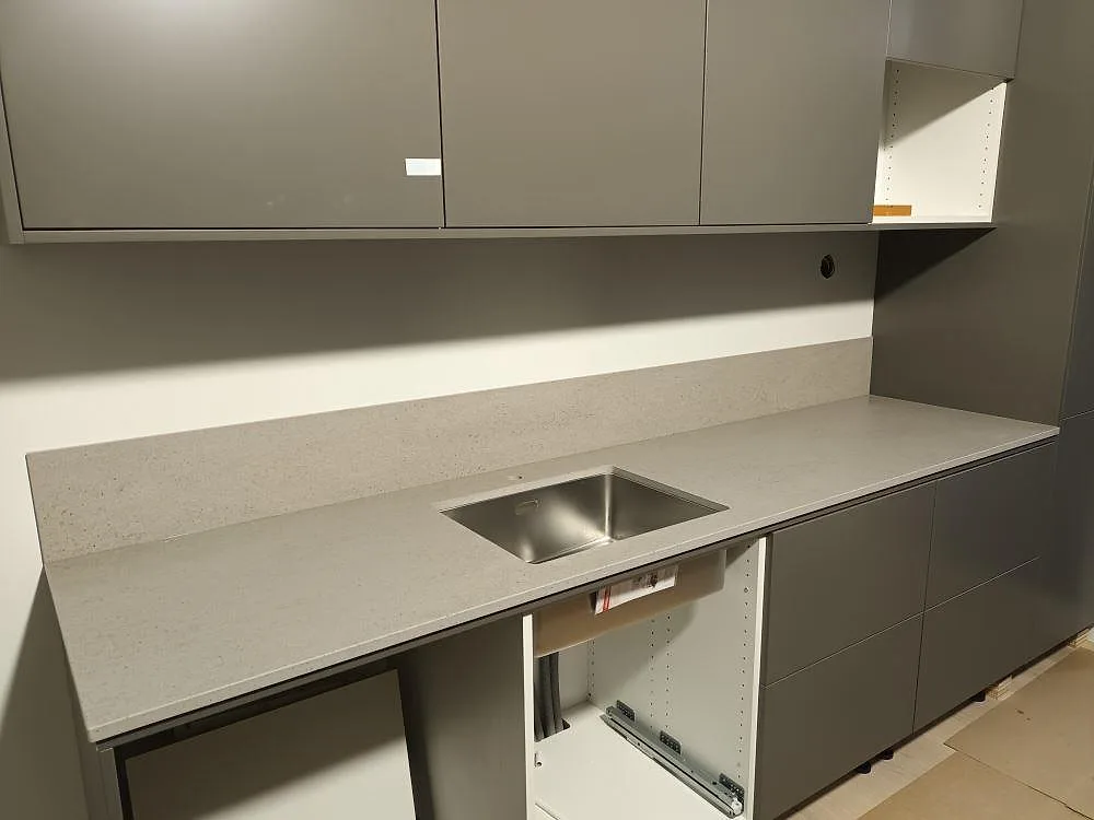 Närbild på matt Dekton Strato köksbänkskiva med rostfri diskho och låg stänkkant mot grå köksskåp i Svärdsklova.