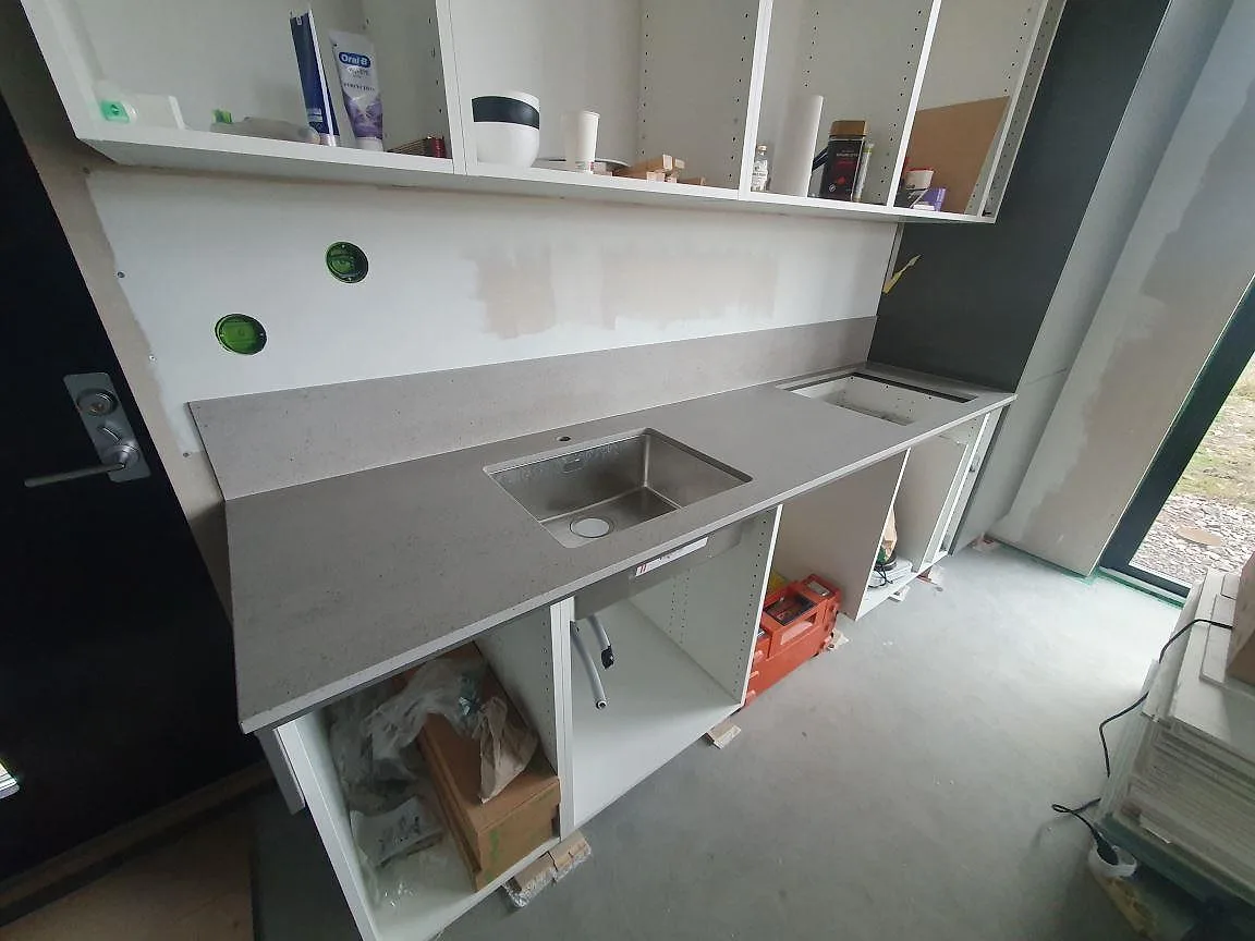 Köksbänkskiva i grå Dekton Strato med underlimmad diskho och uppvikt stänkskydd i samma keramiksten i ett kök i Svärdsklova Nyköping.