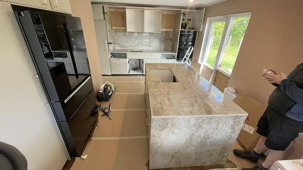 Köksö och väggbänkar i polerad Dekton Taga keramik med gråbeige ådring under montering i ett kök i Anderslöv.