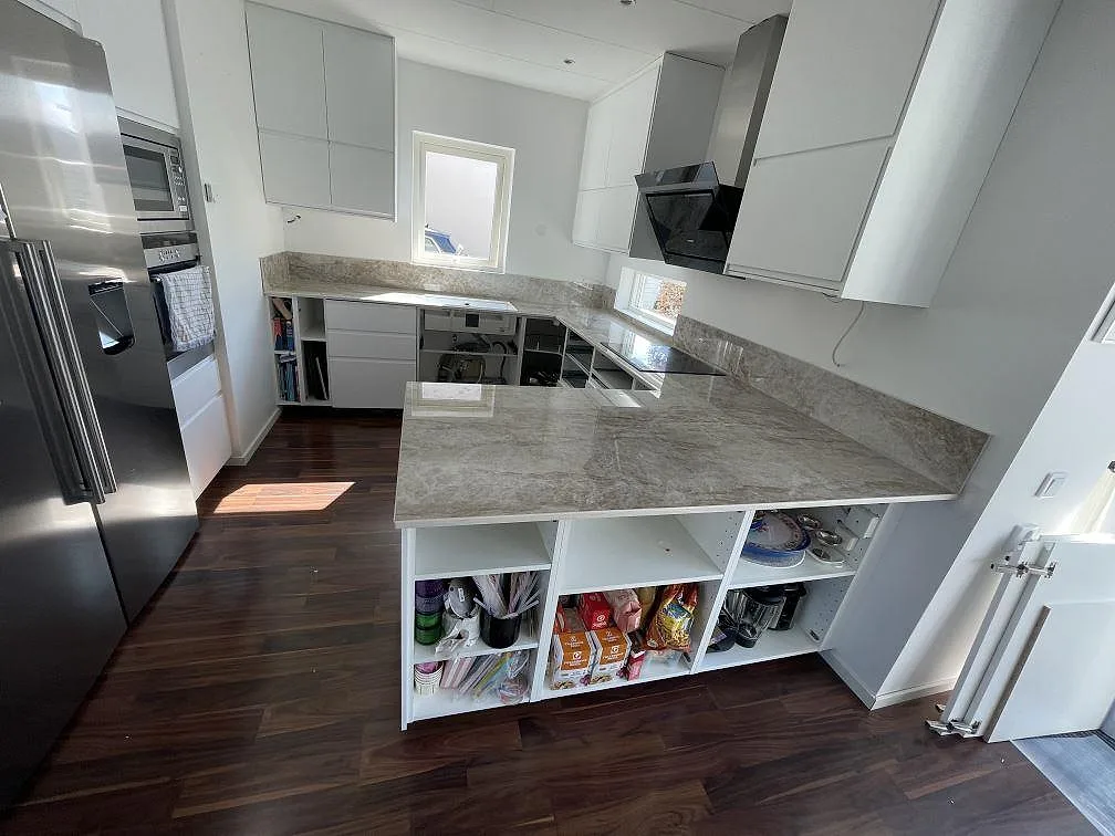Översiktsbild av U-format kök med köksbänkskiva i Dekton Taga, polerad varmbeige sintrad sten, häll och rostfritt kylskåp i Bunkeflostrand.