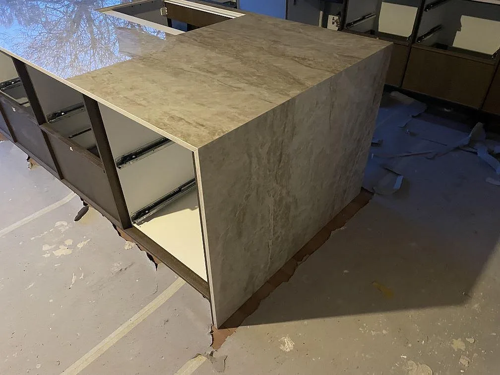 Polerad köksö i Dekton Taga med waterfall-kant ner till golvet, beige keramikyta med diskret ådring, sett snett uppifrån i ett kök i Gentofte.
