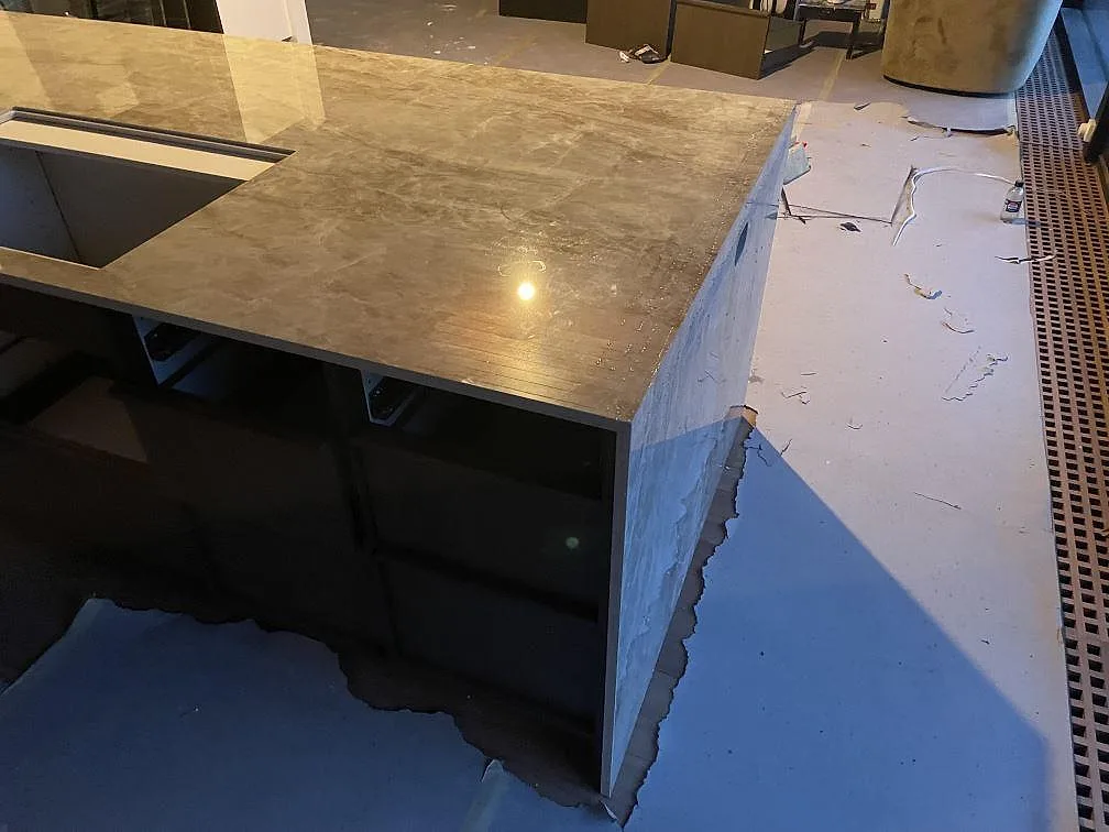 Köksö i polerad Dekton Taga med nedfälld stenkant och öppna stommar under, beige keramik i cementlook i ett kök i Gentofte.