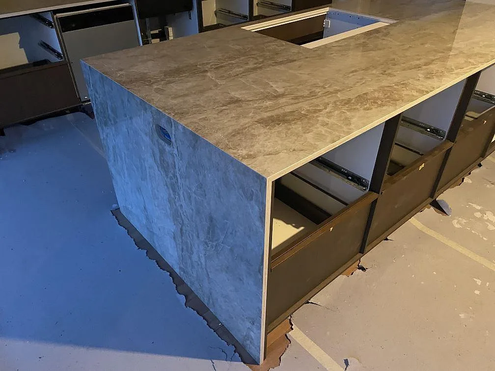 Köksbänkskiva i Dekton Taga, polerad beige keramik med cementlook, på en U-formad köksö med heltäckande nedfälld sida i ett kök under montering i Gentofte.