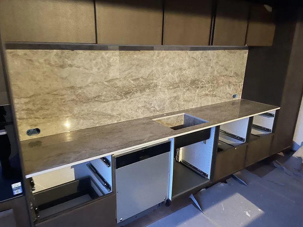 Heltäckande stänkvägg och bänkskiva i Dekton Taga längs köksrad med urtag för diskho och integrerad diskmaskin i ett kök under montering i Gentofte.