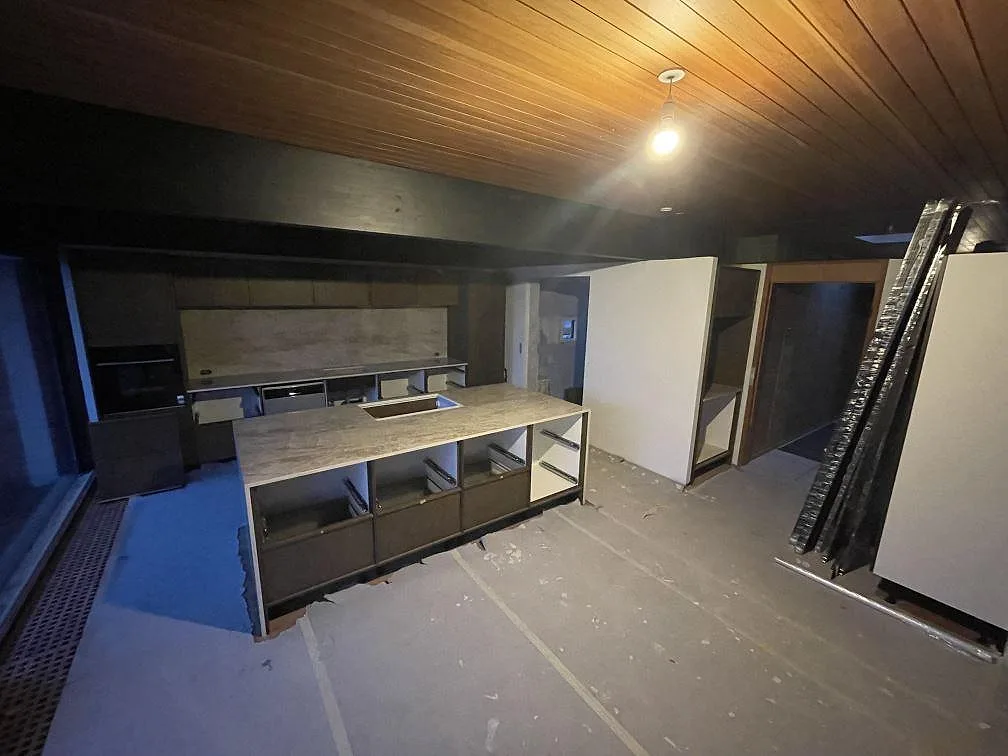 Översikt av ett kök under montering i Gentofte med köksö och köksrad i Dekton Taga, beige keramikbänkskivor under trätak.