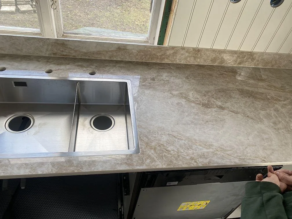 Ovanifrån på underlimmad rostfri dubbeldiskho i bänkskiva av Dekton Taga vid fönster i ett kök i Göteborg.