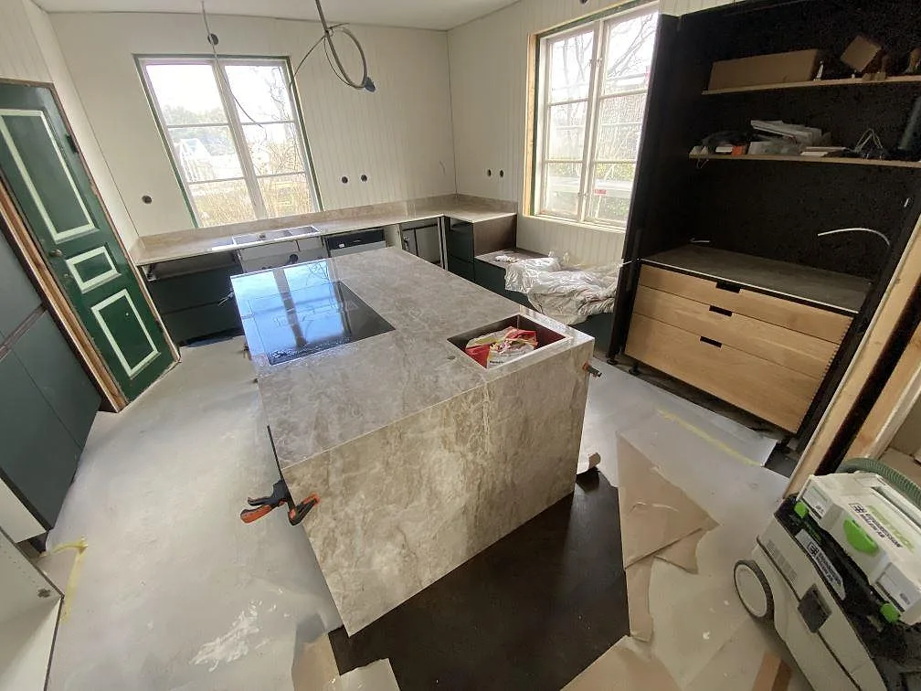 Köksbänkskiva och köksö i Dekton Taga, polerad keramik i varm beige ton, monterad i ett kök med gröna luckor i Göteborg.