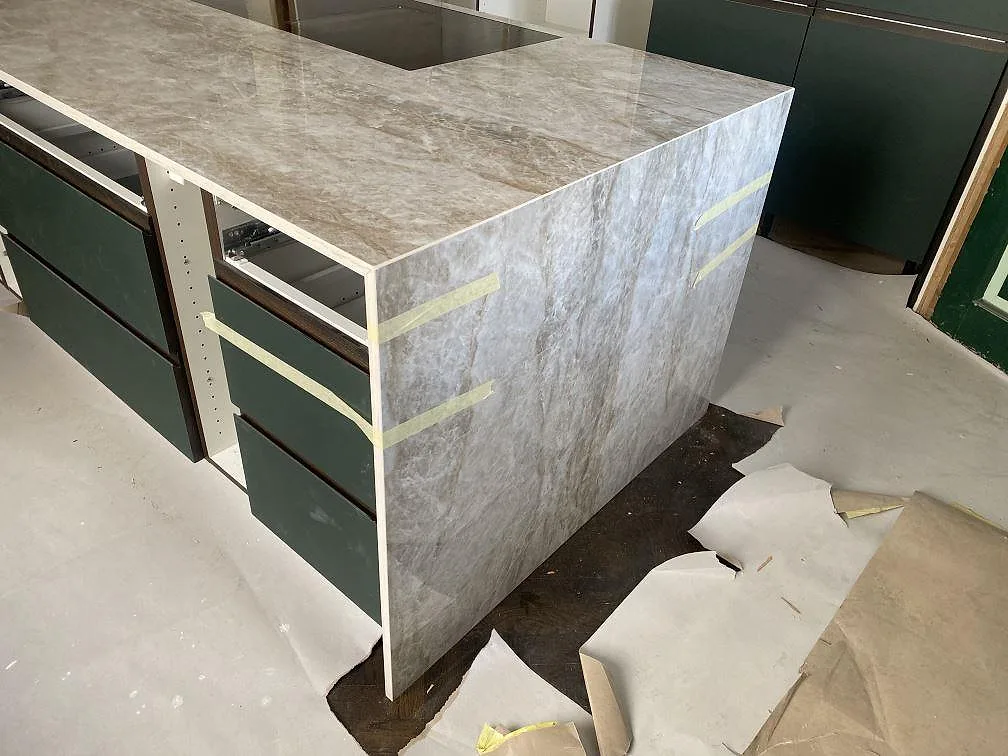 Köksö i Dekton Taga med nedvikt sidopanel i samma keramik mot gröna lådfronter, polerad yta, i ett kök i Göteborg.