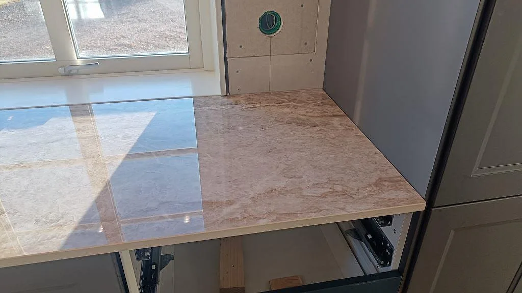 Polerad Dekton Taga bänkskiva i ett kök i Grästorp där dagsljus speglas i den blanka keramikytan vid fönstret.