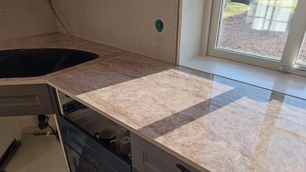 Eklevel-bild av polerad Dekton Taga köksbänkskiva i Grästorp med infälld svart kompositdiskho och stänkvägg i keramik, fotograferad under montering.