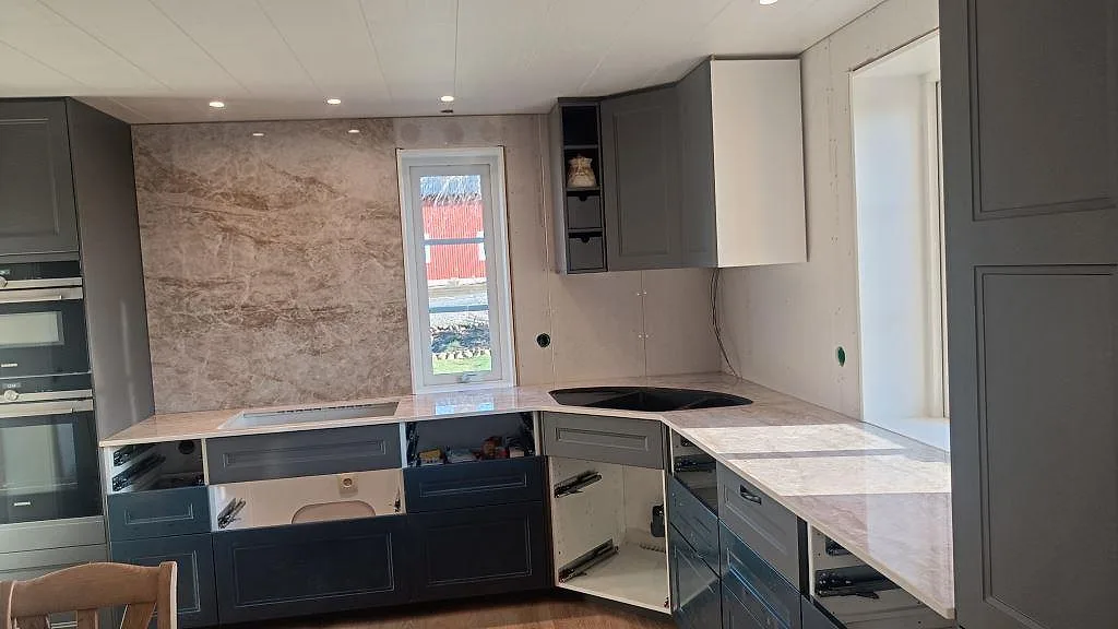 Köksbänkskiva i Dekton Taga, polerad keramik i varm jordton, installerad i ett vinkelkök i Grästorp med induktionshäll och stänkvägg i samma sten under montering.