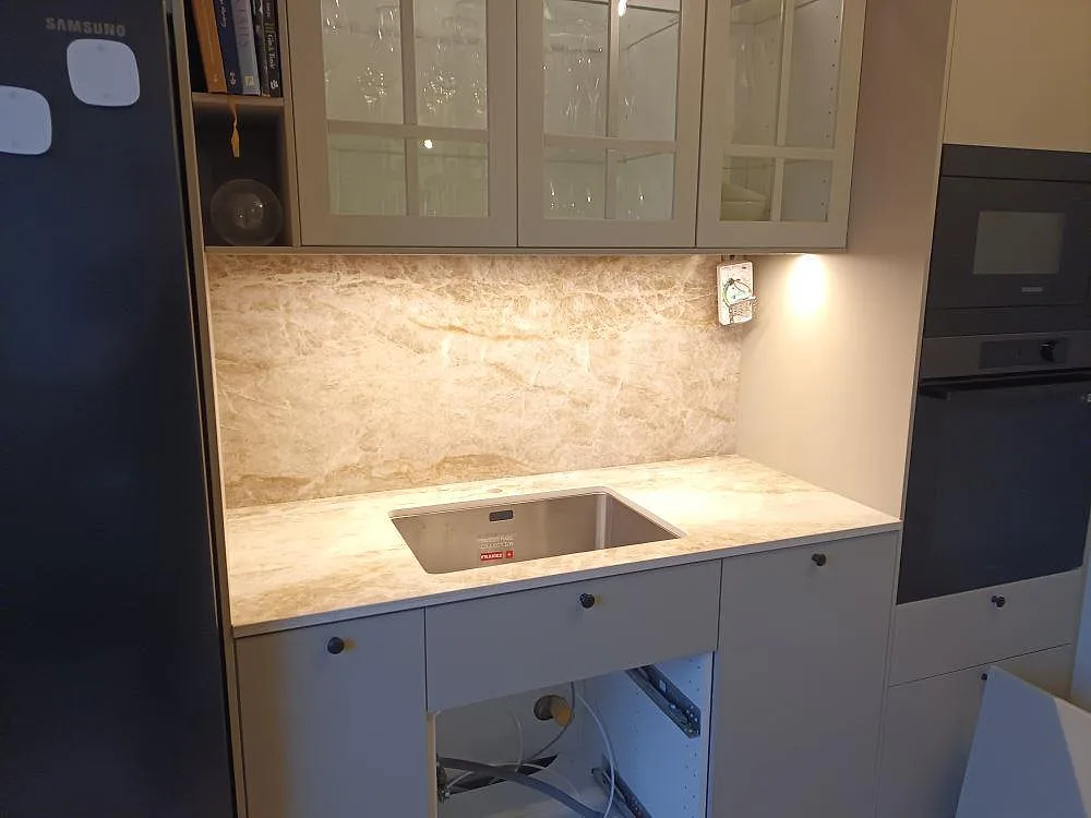 Köksbänkskiva i Dekton Taga, polerad keramik i varm beige travertinlook, med underlimmad rostfri diskho och uppvikt stänkskydd i ett kök i Hägersten.