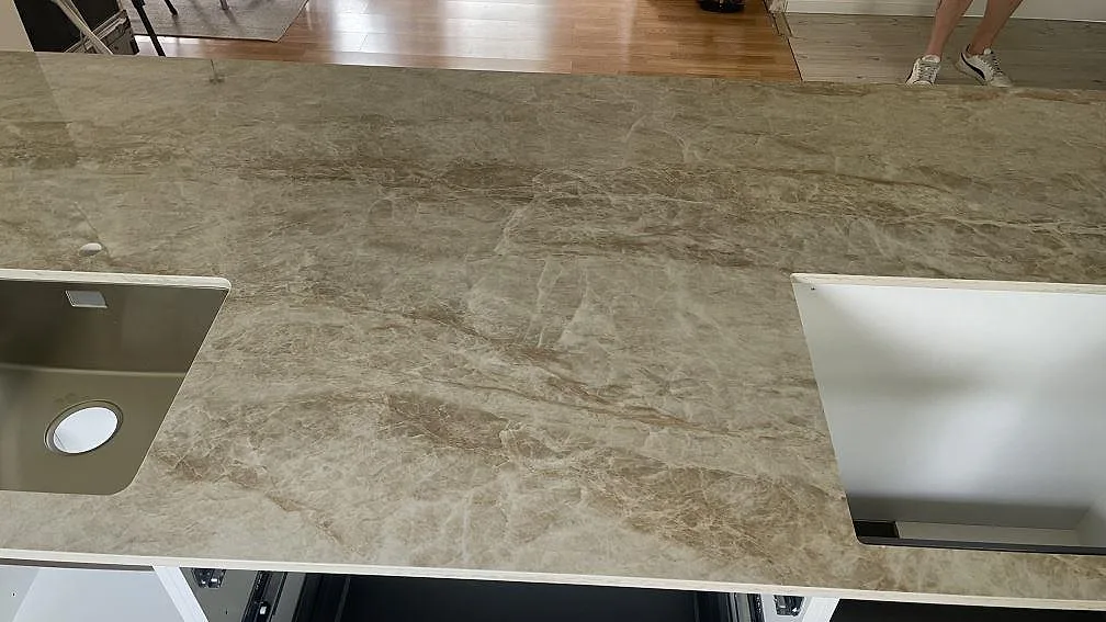 Topbild av köksbänkskiva i polerad Dekton Taga med rostfri diskho, hällurtag och gråbeige marmorlik ådring i Hässleholm.