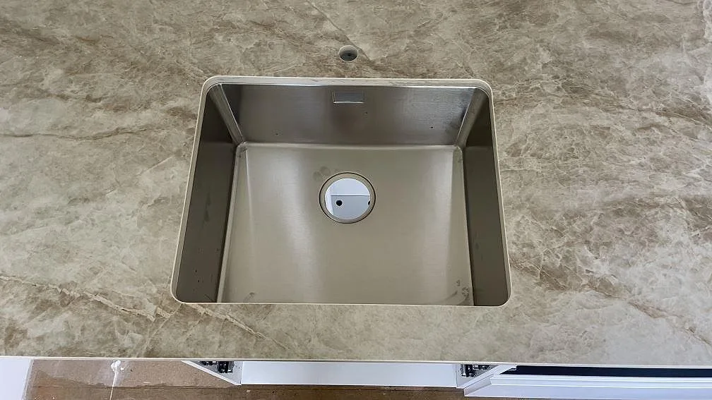 Rostfri diskho i köksbänkskiva av polerad Dekton Taga, gråbeige keramik med ljus ådring, i ett kök i Hässleholm.