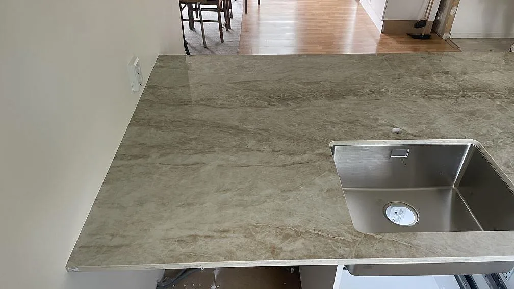 Köksbänkskiva i polerad Dekton Taga vid vägg med rostfri diskho och varm gråbeige ådring i Hässleholm.