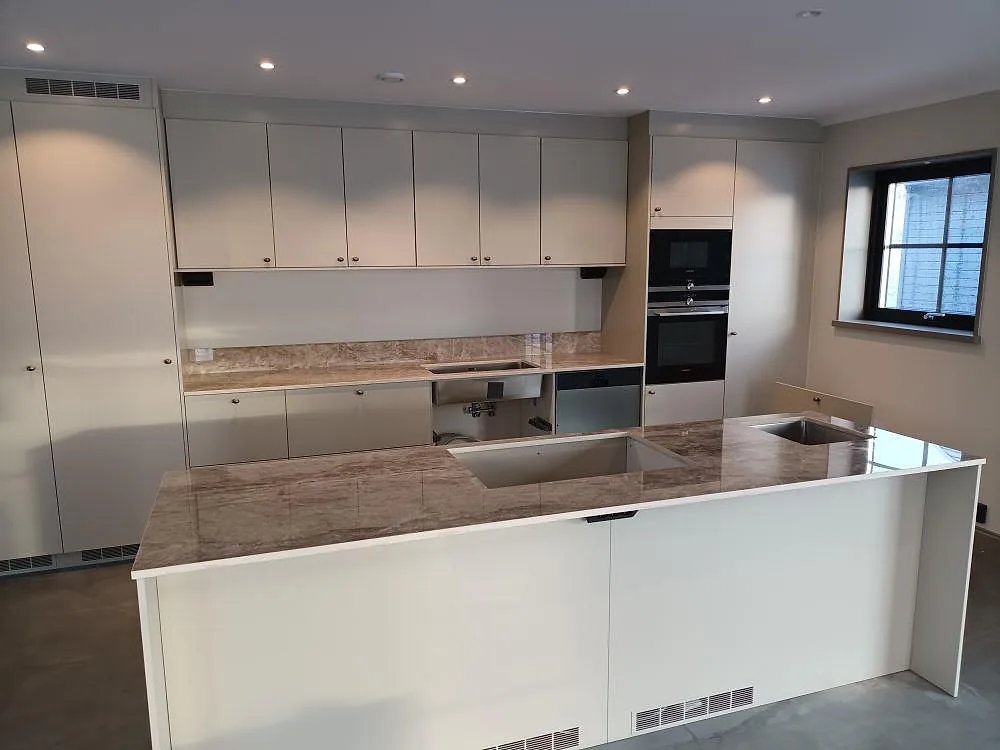 Köksbänkskiva och köksö i Dekton Taga, ljus krämbeige keramik med travertinådring, i ett kök under montering i Hedemora.