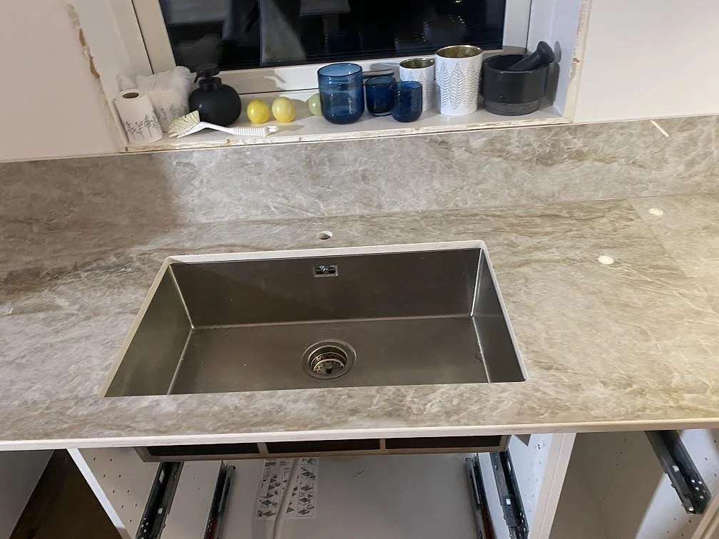 Underlimmad rostfri diskho i en polerad Dekton Taga bänkskiva med uppvikt stänkskydd i kök i Hindås.