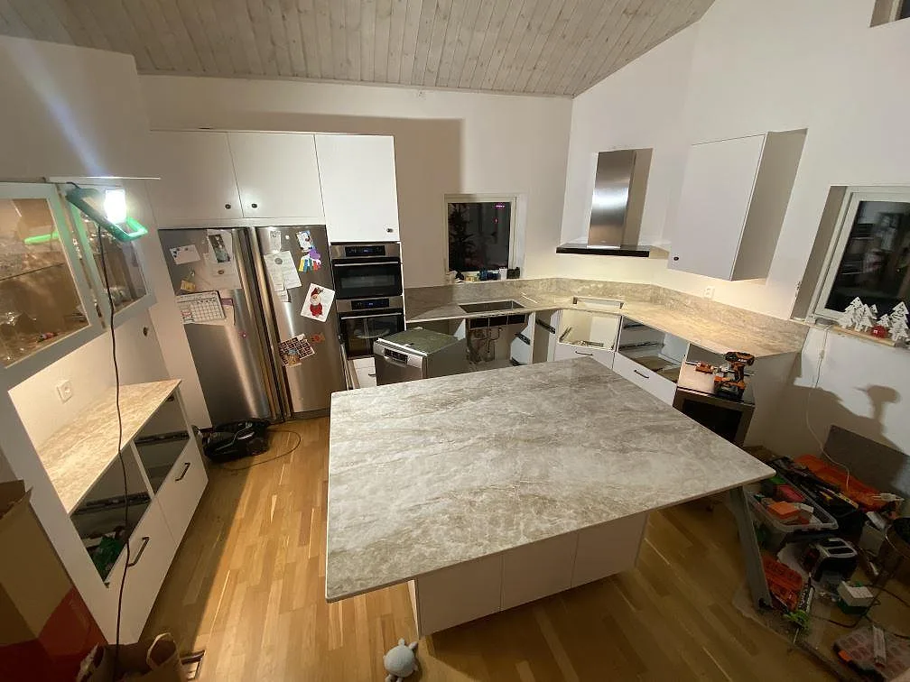 Köksbänkskiva och köksö i polerad Dekton Taga med gråbeige ådring i ett kök under montering i Hindås.